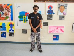 5.-Dr.-Adeola-Shobo-stands-in-front-of-artworks-featured-in-the-Cultivating-Legacy-exhibition